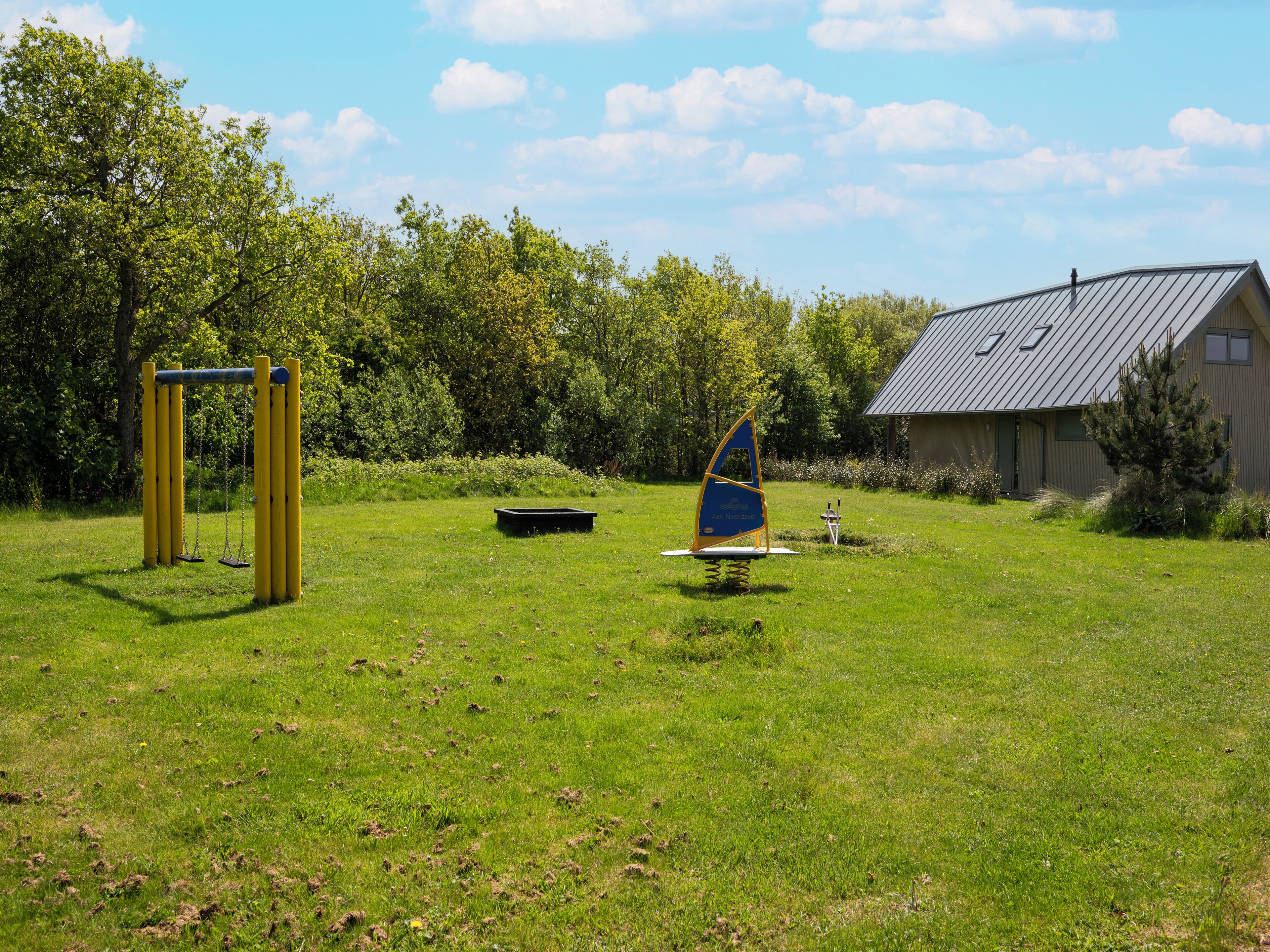 A grassy outdoor area with playground equipment, a sailboat, and a building with a sloped roof.