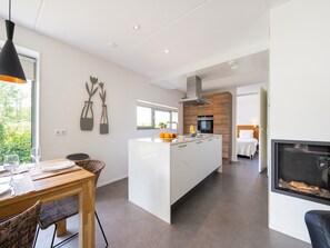 Una cucina moderna con isola centrale, zona pranzo con tavolo e sedie e angolo living con camino.