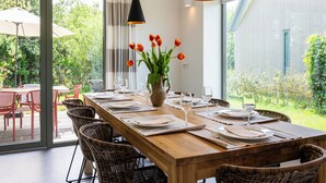 A dining area with a wooden table set for six, surrounded by wicker chairs, with a vase of tulips on the table.