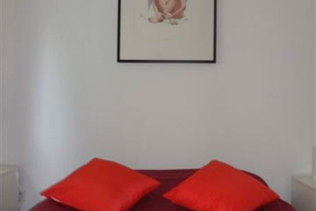 A room with a bed, two red pillows, and a framed picture on the wall.