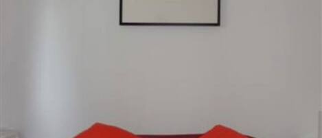 A room with a bed, two red pillows, and a framed picture on the wall.