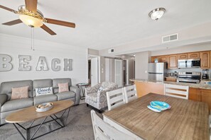 A modern living room with a gray sofa, a wooden dining table, and a ceiling fan. - Seaside Beach & Racquet 3706 by Liquid Life (Orange Beach)