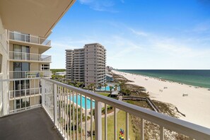 Varanda com vista para uma praia, uma piscina e um edifício alto.