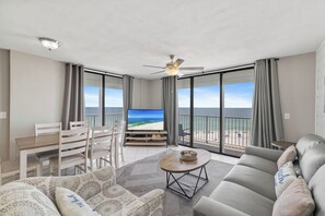 A living room with a TV, sofa, and dining area, overlooking a beach. - Seaside Beach & Racquet 3706 by Liquid Life (Orange Beach)