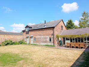 A brick building with a sloped roof, a small attached structure with a green door, and a grassy yard with outdoor seating.
