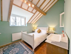 A bedroom with a sloped ceiling, a bed, a nightstand, a bedside lamp, a window, a radiator, and a bathroom with a sink.