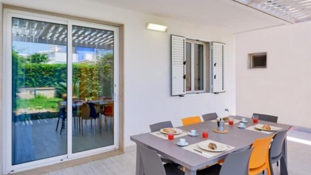 A modern dining area with a large table and chairs, a sliding glass door leading to an outdoor patio, and a ceiling with a white lattice design. - Ibiscus-Iblee, holiday home with garden 100 mt from the sea (Marina di Ragusa)