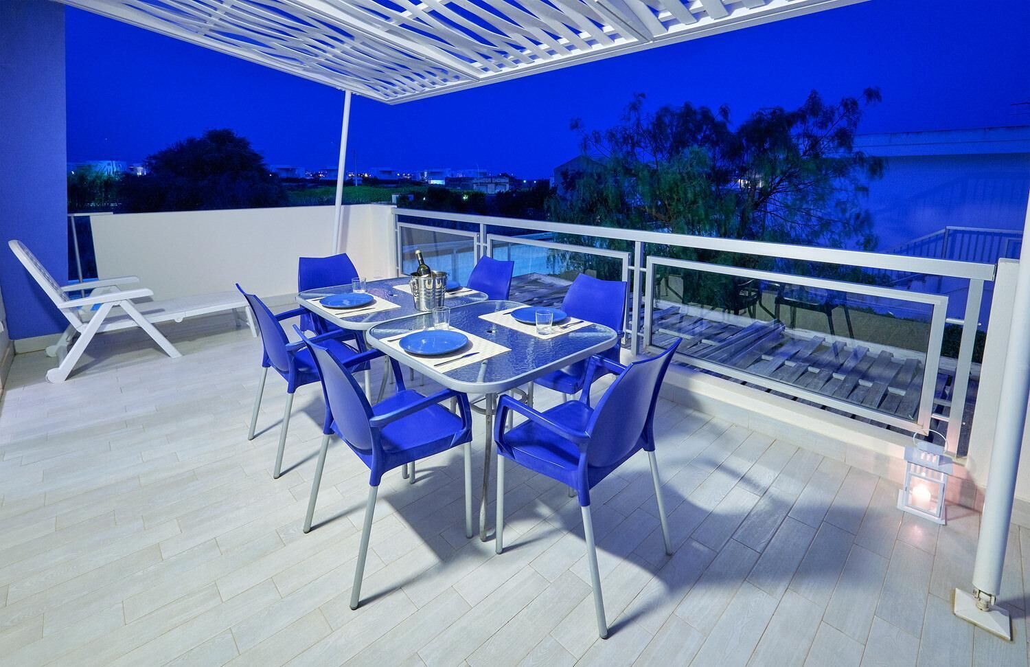 A rooftop terrace with a table and chairs, a pergola, and a view of the cityscape at dusk.
