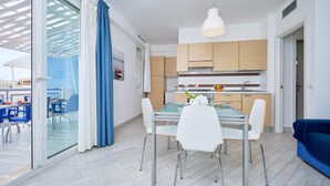 Moderni keittiö, jossa on puiset kaapit, lasinen ruokapöytä ja sininen sohva.