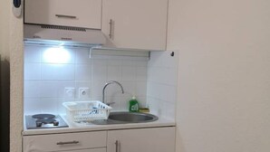 A compact kitchen with white cabinets, a stainless steel sink, a dish rack, and a gas stove.