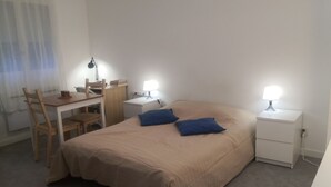 A bedroom with a bed, two bedside tables with lamps, a desk with a chair, and a window with curtains.