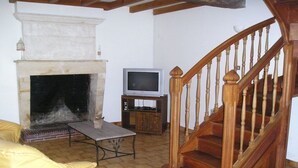 Ein Wohnzimmer mit Kamin, einem Fernseher auf einem Schrank, einer Holztreppe und einem gelben Sofa.