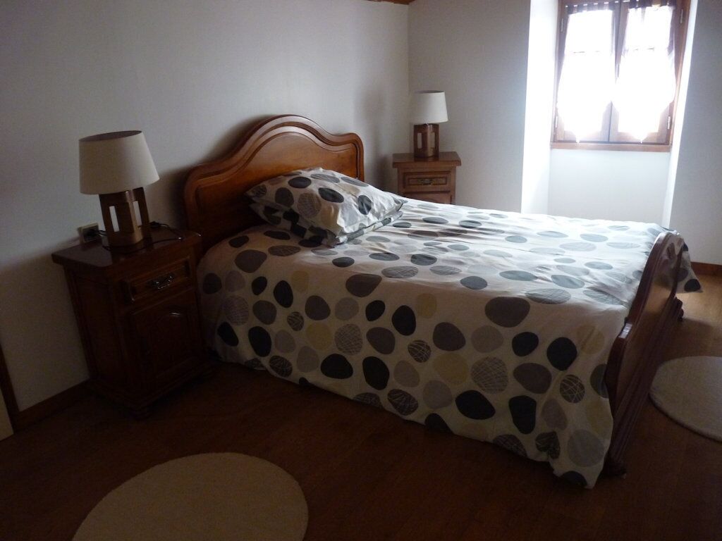 A bedroom with a bed, two bedside tables, a nightstand, and a window with curtains.