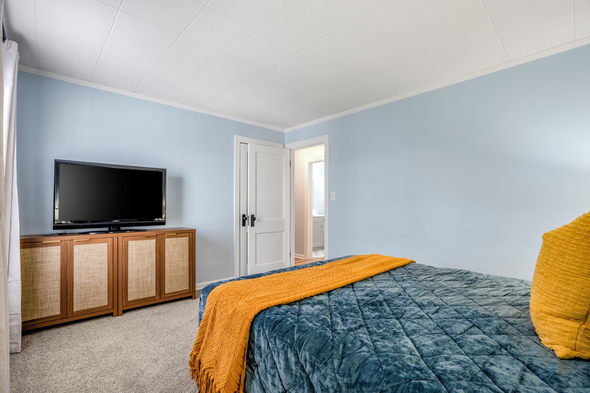 A bedroom with a bed, a television on a wooden cabinet, and a door leading to another room.