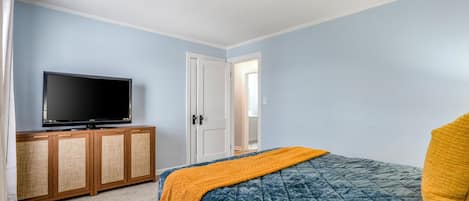 A bedroom with a bed, a television on a wooden cabinet, and a door leading to another room.