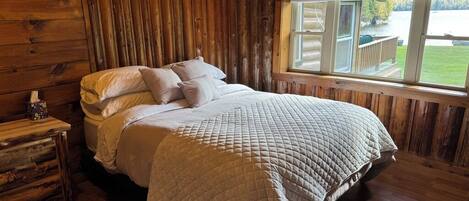 Une chambre dans une cabane en bois, avec un lit, une table de chevet et une fenêtre donnant sur un lac.