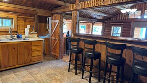 Een rustiek houten interieur met een bar, houten krukken en een bord waarop 