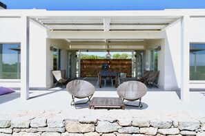Een overdekt terras met twee loungestoelen, een tafel en een stenen muur.