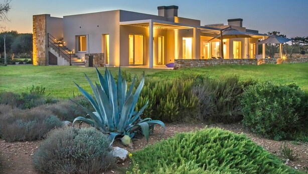 Una casa moderna con fachada de piedra, amplios ventanales y un jardín bien cuidado.
