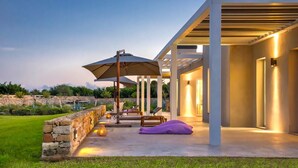 Un patio moderno al aire libre con pared de piedra, sillones de descanso y una pérgola con sombrilla.