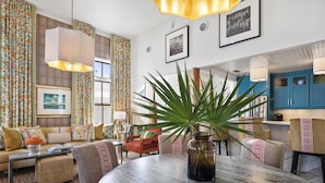 Un salón con una mesa redonda, sofás y una planta grande en maceta.