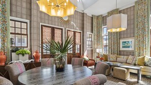Amplia sala de estar con una mesa redonda de madera, asientos cómodos y elementos decorativos como cortinas estampadas y una lámpara con forma de sol.