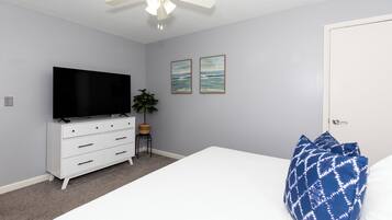 A bedroom with a bed, a TV on a dresser, a ceiling fan, and two framed pictures on the wall.