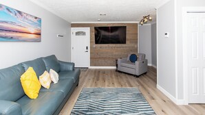 A modern living room with a blue sofa, a patterned rug, and a wooden accent wall.