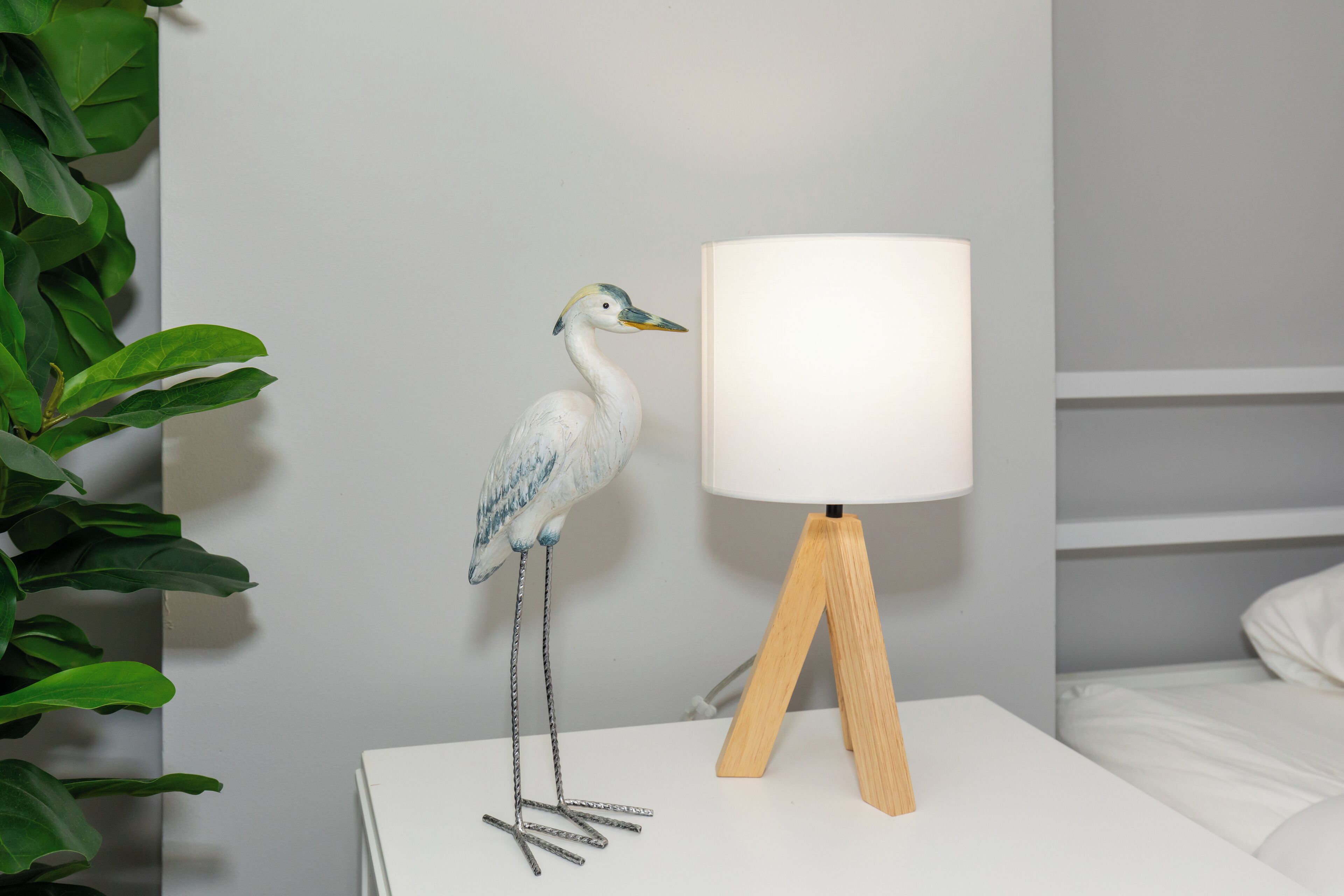 Ein weißer Nachttisch mit Lampe und einer dekorativen Vogel-Skulptur.
