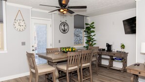A dining area with a wooden table and chairs, a ceiling fan, a clock, and a coffee bar.