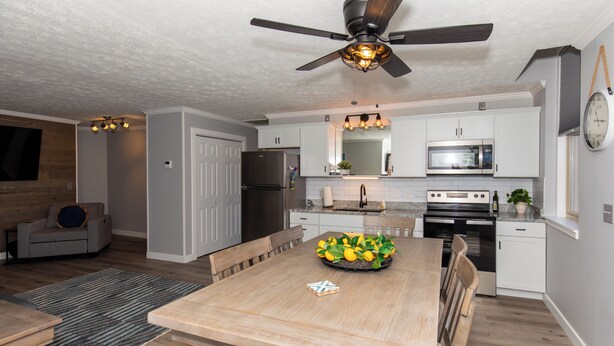 A modern kitchen with white cabinets, a wooden dining table, and a ceiling fan.