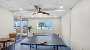 A ping pong table in a room with a ceiling fan, large windows, and a view of the outside.