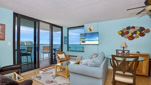 A living room with a light blue couch, a glass coffee table, and a dining area with a wooden table and chairs.