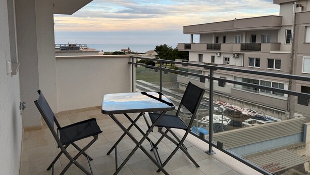 Ein Balkon mit Tisch und Stühlen, mit Blick auf ein Wohngebiet und ein Gewässer.