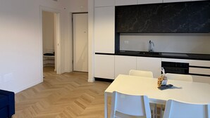 Eine moderne Küche mit weißen Schränken, einer schwarzen Marmor-Spritzschutzwand und einem weißen Esstisch mit Stühlen.