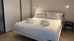 Ein modernes Hotelzimmer mit einem großen Bett, weißen Bettwäsche und einem kleinen Nachttisch.