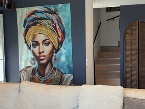 A room with a large painting on the wall, a staircase, and a closed wooden door.