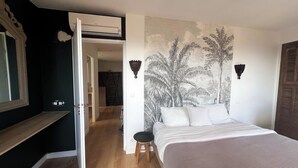 Un dormitorio con una cama, una mesita de noche, una lámpara de pared y una puerta que da a otra habitación.