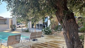 Una terraza de madera con piscina, sillones de descanso y un árbol.