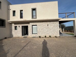 Un edificio moderno su due piani, con facciata in pietra, patio coperto e vialetto in ghiaia.