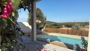 Un área de piscina con terraza de madera, sillas de descanso y vistas del paisaje circundante.