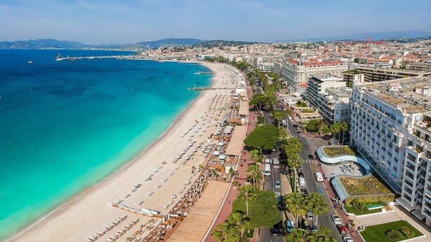 Vista aérea de una ciudad costera con una playa extensa, un puerto deportivo y edificios modernos.