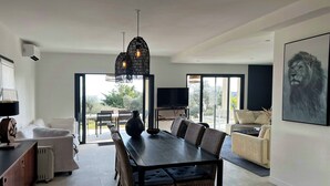Una sala moderna con comedor, sofá, televisor y un amplio ventanal que ofrece vistas al exterior.