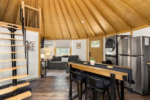 A compact kitchen with a wooden ceiling, a dining area with a table and chairs, a sofa, and a refrigerator.