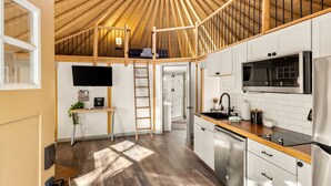 A compact kitchen with a wooden ceiling, a TV, a microwave, and a dishwasher. - Stetson + Bronco: 2 Lux Connected Yurts | 5bds 2ba (Canyon Lake)