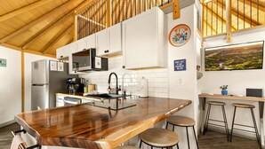 Una cocina moderna con una isla de madera, taburetes, microondas y un ventanal grande.