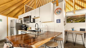 Una cocina moderna con una isla de madera, taburetes, microondas y un ventanal grande.