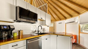 Una cocina compacta con armarios blancos, lavavajillas de acero inoxidable, microondas y cafetera.