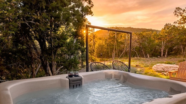 Un jacuzzi rodeado de árboles con un atardecer de fondo.