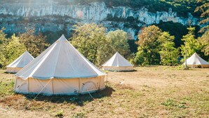 Un camping con varias tiendas de forma cónica instaladas en un campo cubierto de césped, con un risco y árboles al fondo.